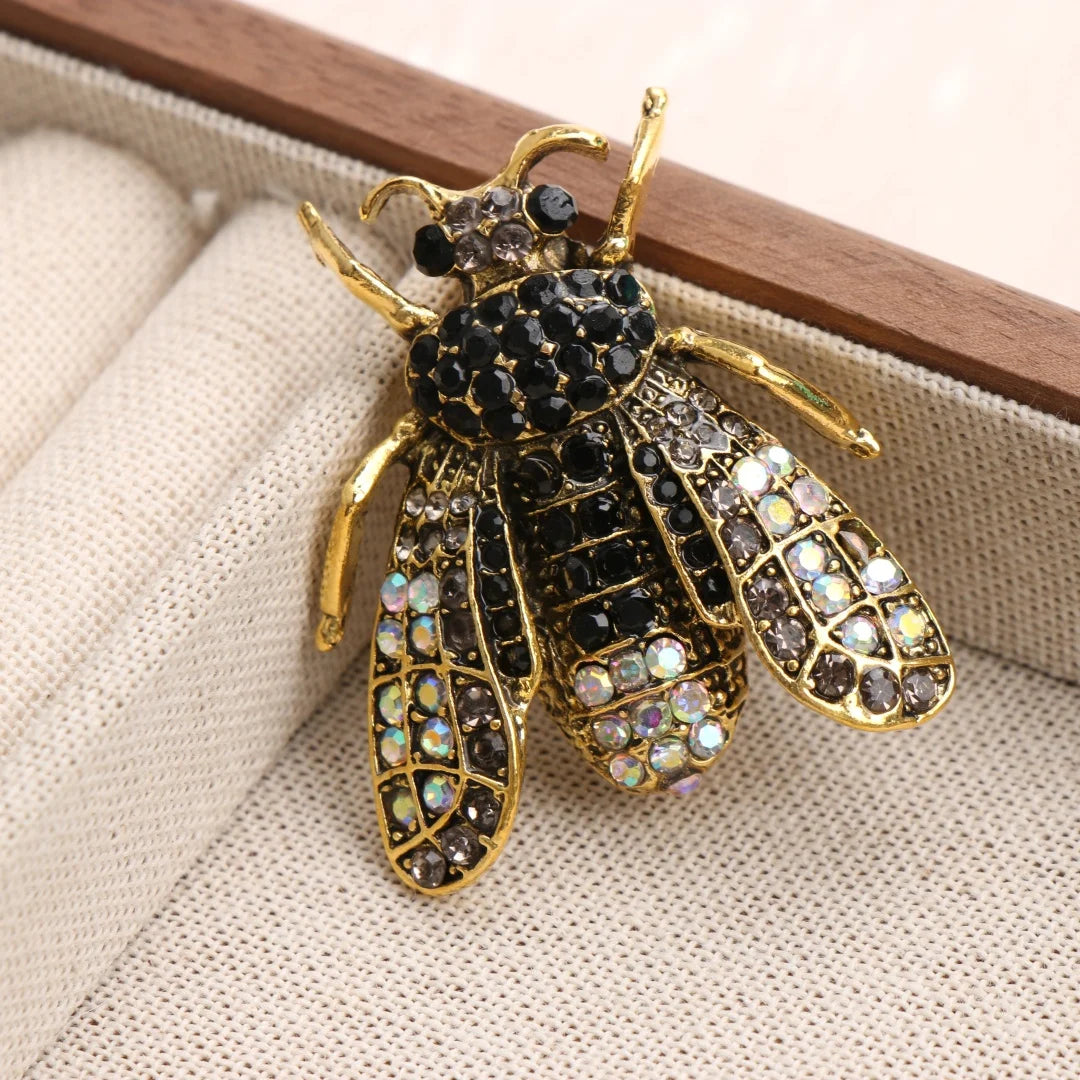 Broche dorée en forme d'abeille avec détails scintillants, présentée sur un fond de tissu clair.