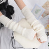 A pair of cream-colored knitted fingerless gloves are displayed on a white surface.
