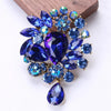 Broche florale en cristal élégante avec des pierres taillées bleu foncé et violet sur fond doré.