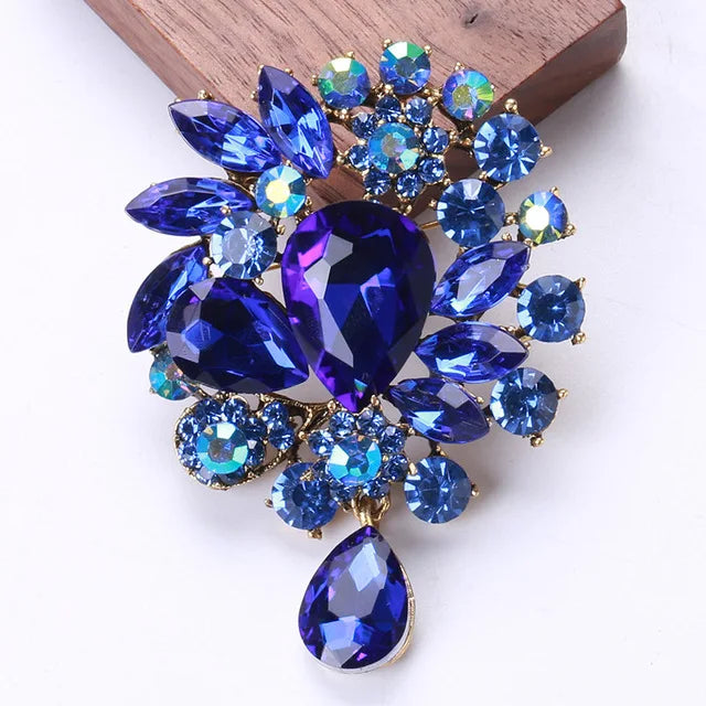 Broche florale en cristal élégante avec des pierres taillées bleu foncé et violet sur fond doré.