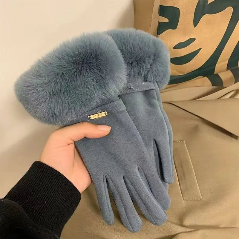 A hand is holding a pair of soft, grey faux fur wrist gloves against a beige fabric background.