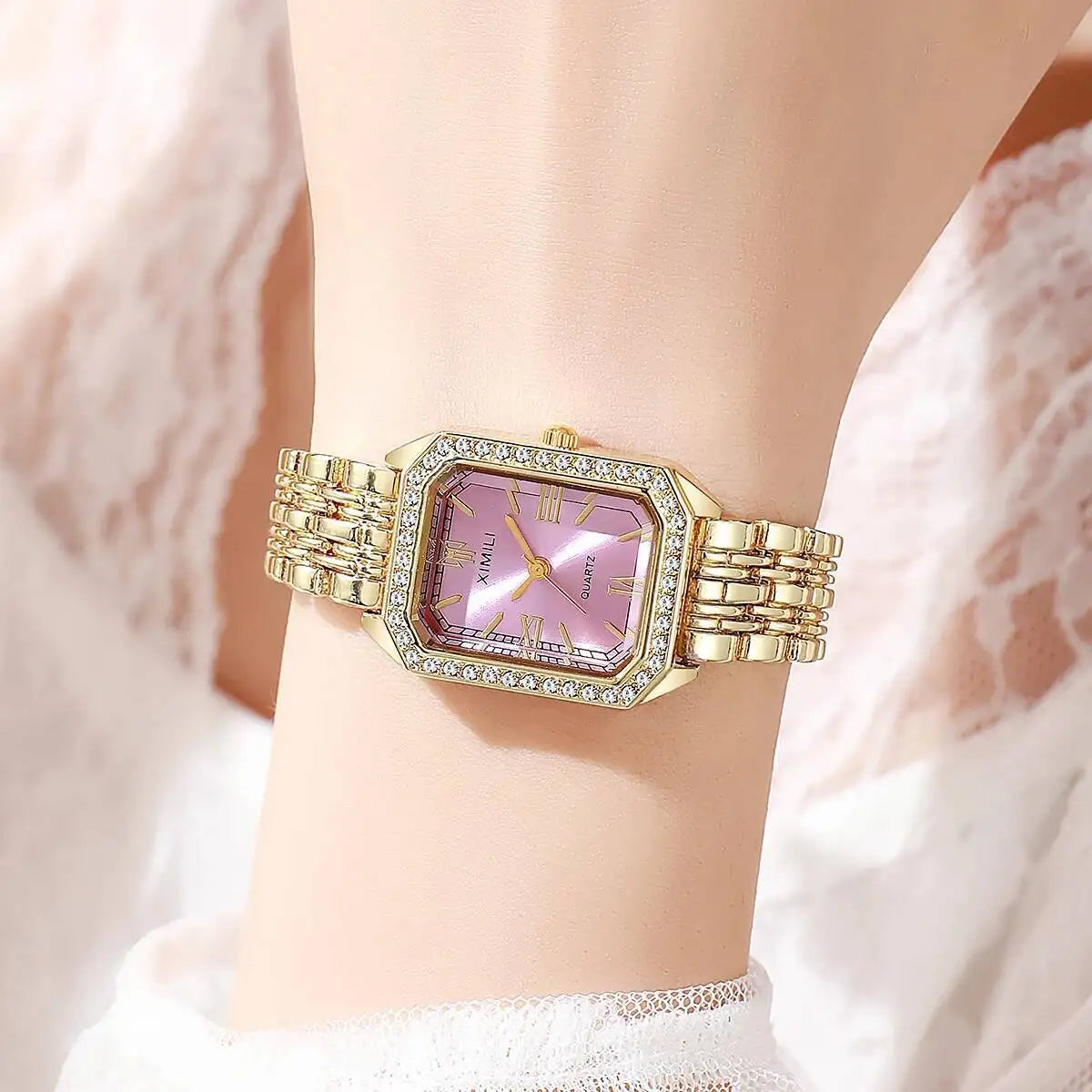 A gold-toned rhinestone quartz wristwatch with a square face and bracelet worn on a wrist.
