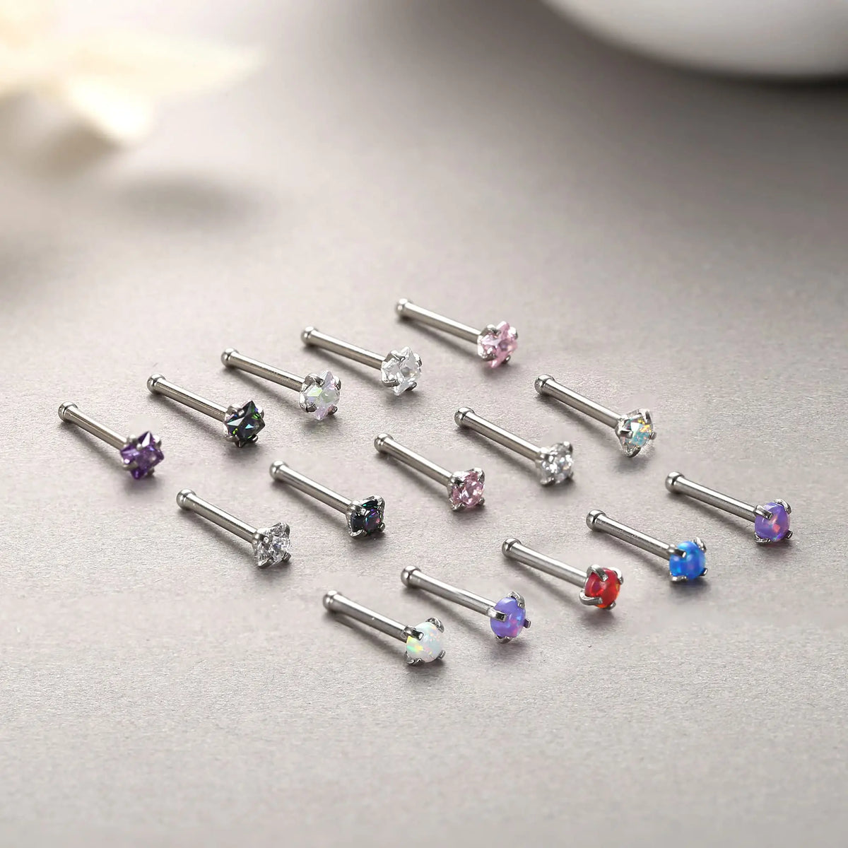 A collection of surgical stainless steel nose piercing studs featuring various colored gemstones like pink, purple, and blue.