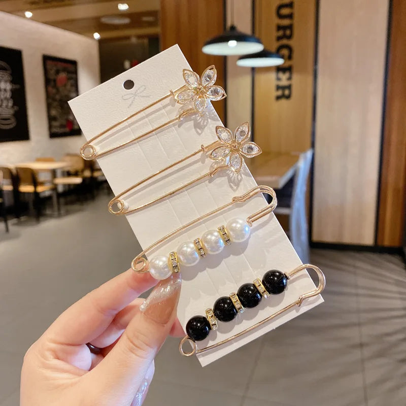 A hand holds a display of gold-toned pearl and black bead brooch pins on a white card.