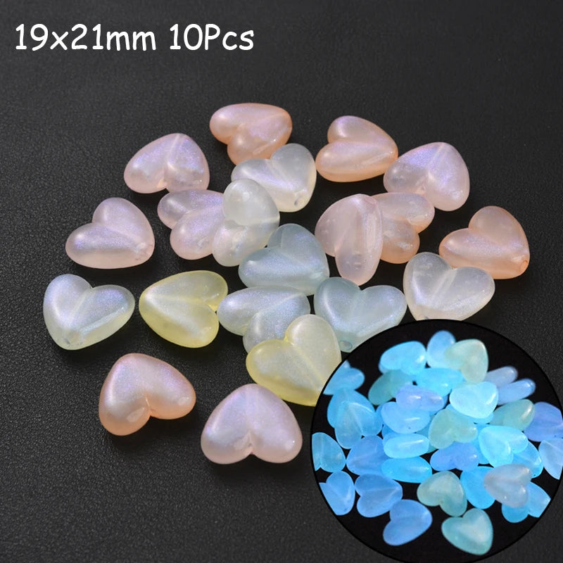 A collection of 10 pink and white glow-in-the-dark acrylic heart-shaped beads scattered on a dark surface.