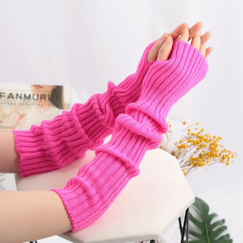 A close-up of bright pink knitted fingerless gloves being worn on a hand against a white background.