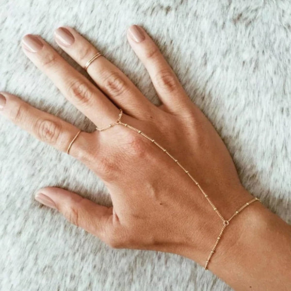 A hand wearing a gold plated link charm bracelet against a light, fuzzy background.