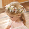 A young girl wears an elegant floral wreath headband with pink and white flowers and greenery.