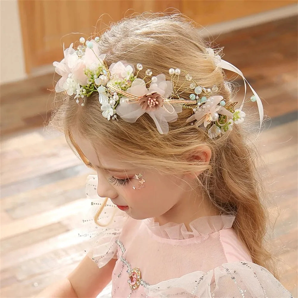 A young girl wears an elegant floral wreath headband with pink and white flowers and greenery.