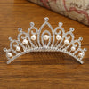 A sparkling crystal princess tiara hair comb adorned with clear stones and pearl drops resting on a wooden surface.