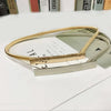 A gold chain waist belt is displayed on a white surface next to some paper and other items.