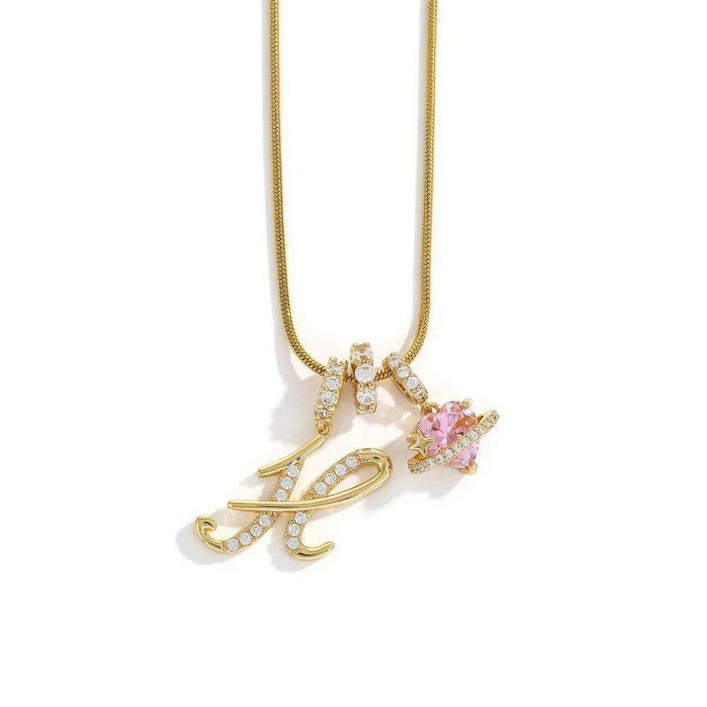 A gold-toned alphabet flower pendant necklace featuring an ornate letter and a pink gemstone accent.