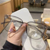 A hand holds a pair of clear anti-blue light eyeglasses resting on a white surface.