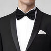 A close-up of a black knit bow tie worn under a black suit jacket with a white shirt.