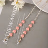 A delicate gold and pink pearl beaded eyewear chain displayed on a gray background.