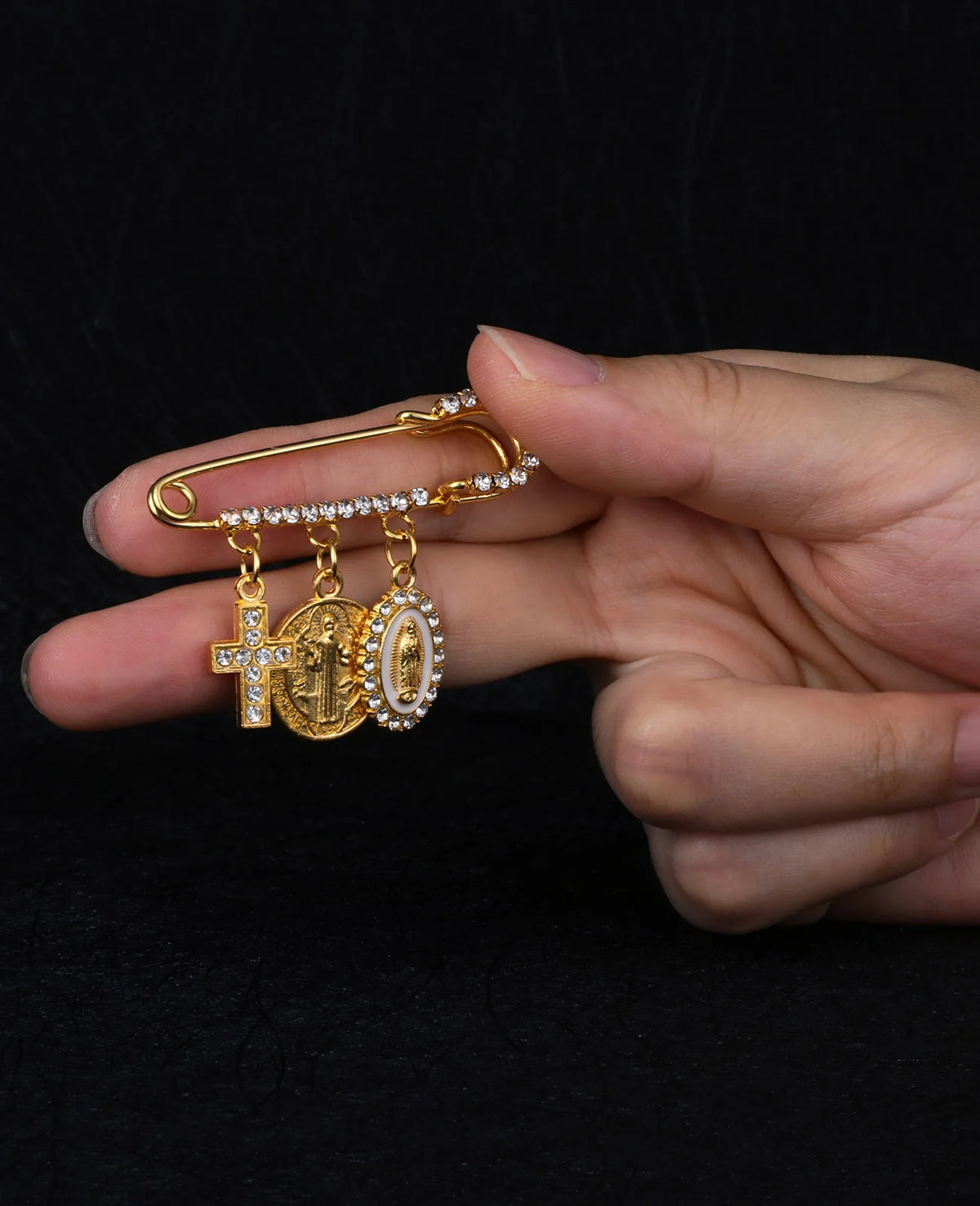 Eine Hand hält eine goldfarbene St. Benedikt-Medaillenbrosche mit Kreuz und der Zahl 10.