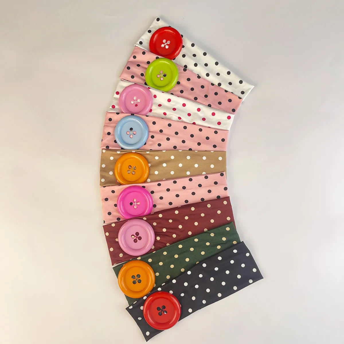 A display of vintage polka dot button headbands in various shades of pink, green, and brown arranged in a fan shape.