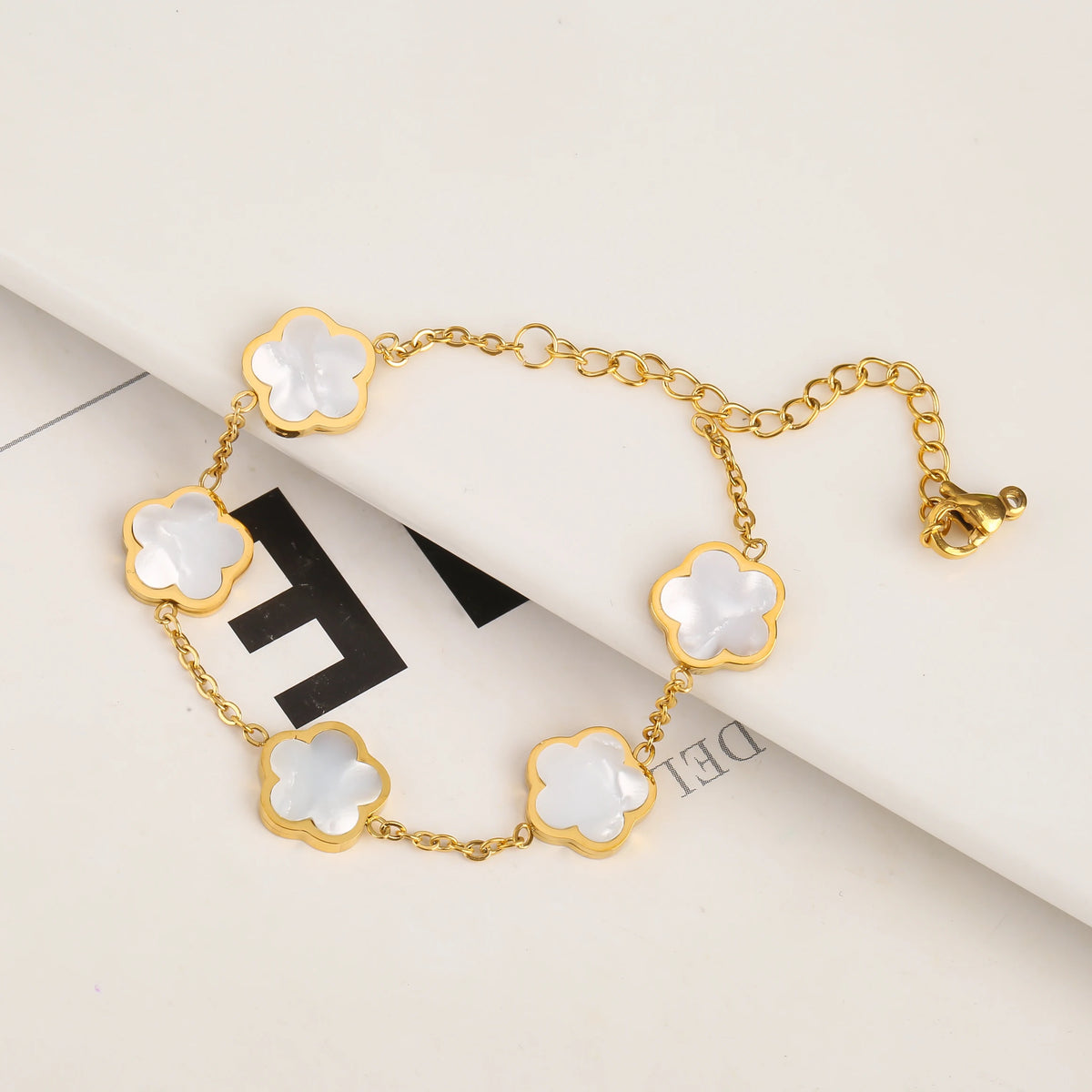 Pulsera de acero inoxidable chapada en oro con pequeños charms de flores blancas en una cadena dorada.
