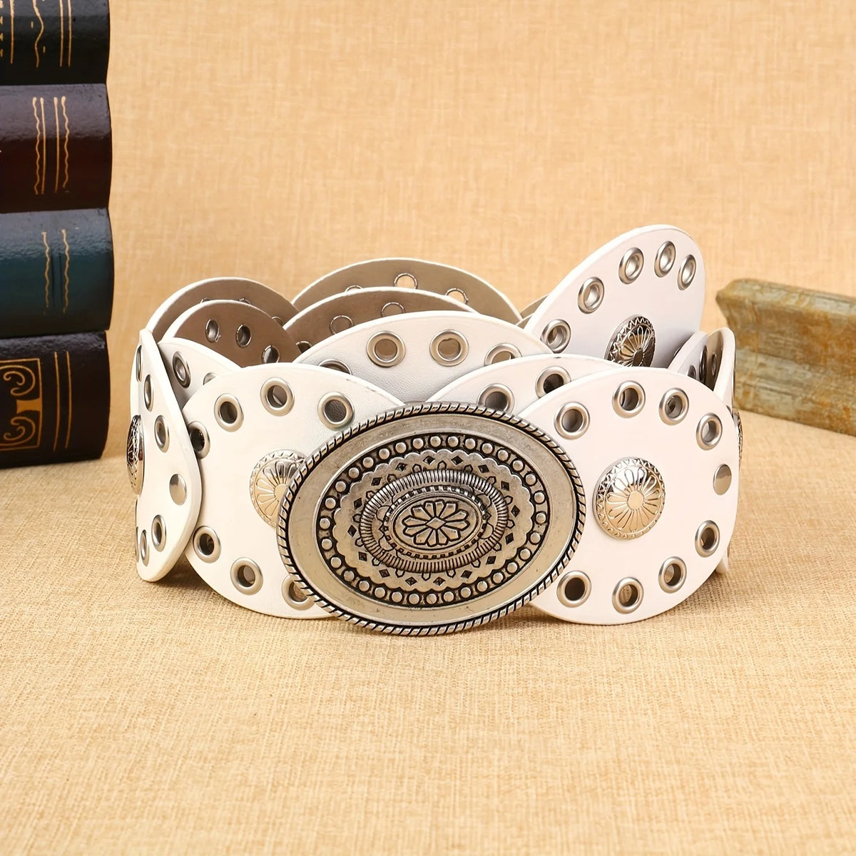 A collection of white and gold floral oval waist belts stacked on a beige fabric surface.