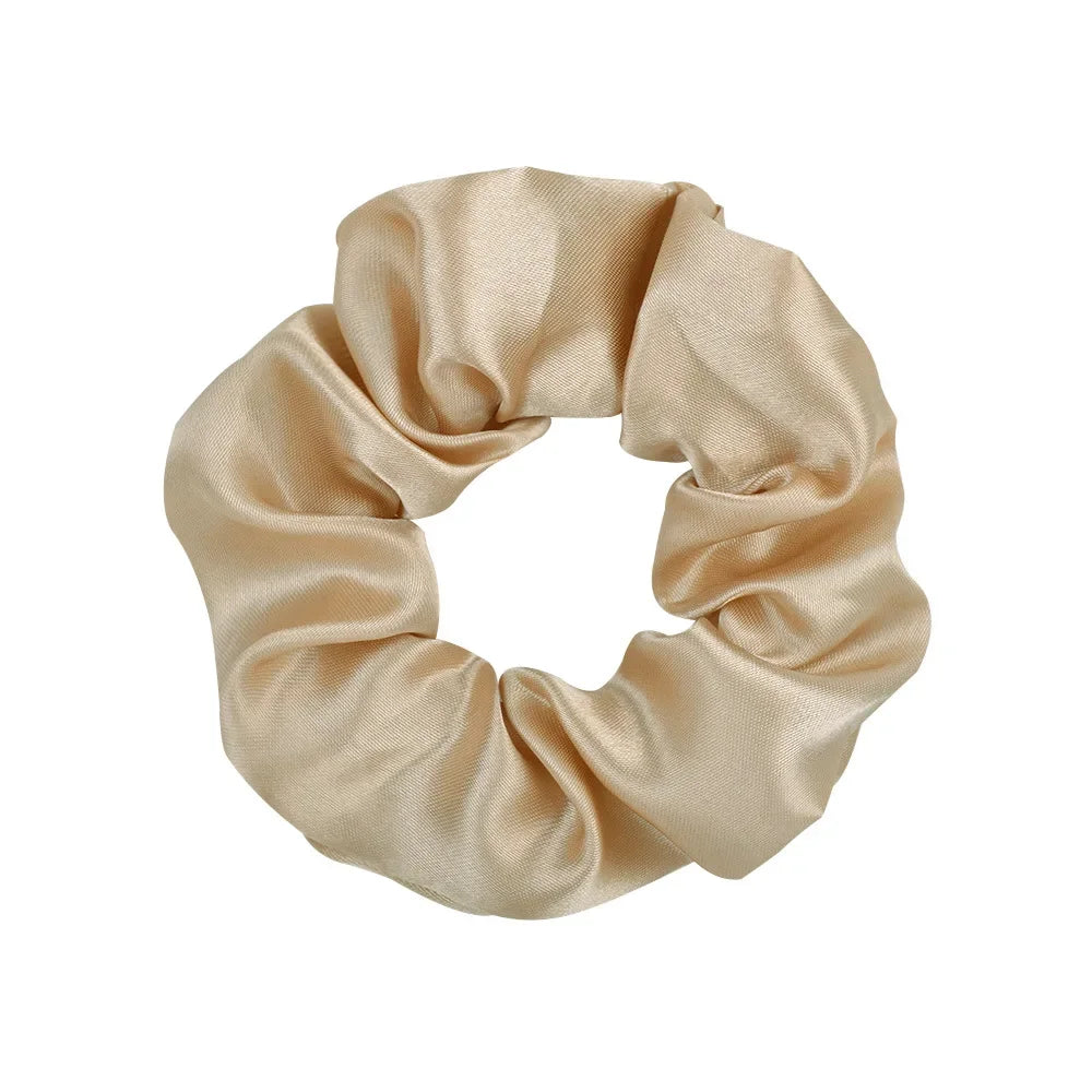 A beige satin fabric scrunchie tied in a gathered, ruched style.