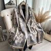 A gray and beige plaid cashmere scarf draped over a hanger against a white background.