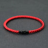 A red braided thread bracelet with a black clasp is displayed on a dark gray surface.