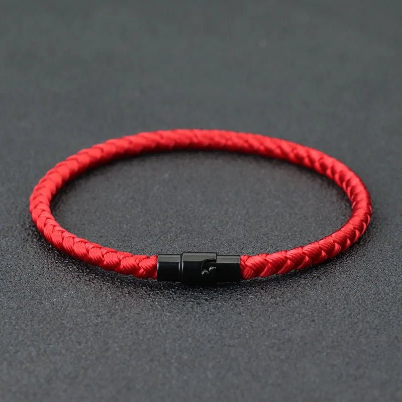 A red braided thread bracelet with a black clasp is displayed on a dark gray surface.