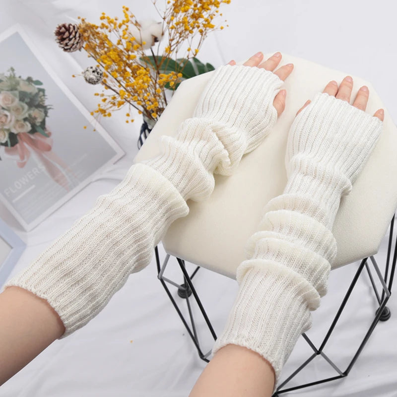 A pair of cream-colored knitted fingerless gloves displayed on a black wire stand.