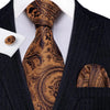 A close-up of a men's silk jacquard tie featuring a brown and gold paisley pattern worn with a dark suit jacket.
