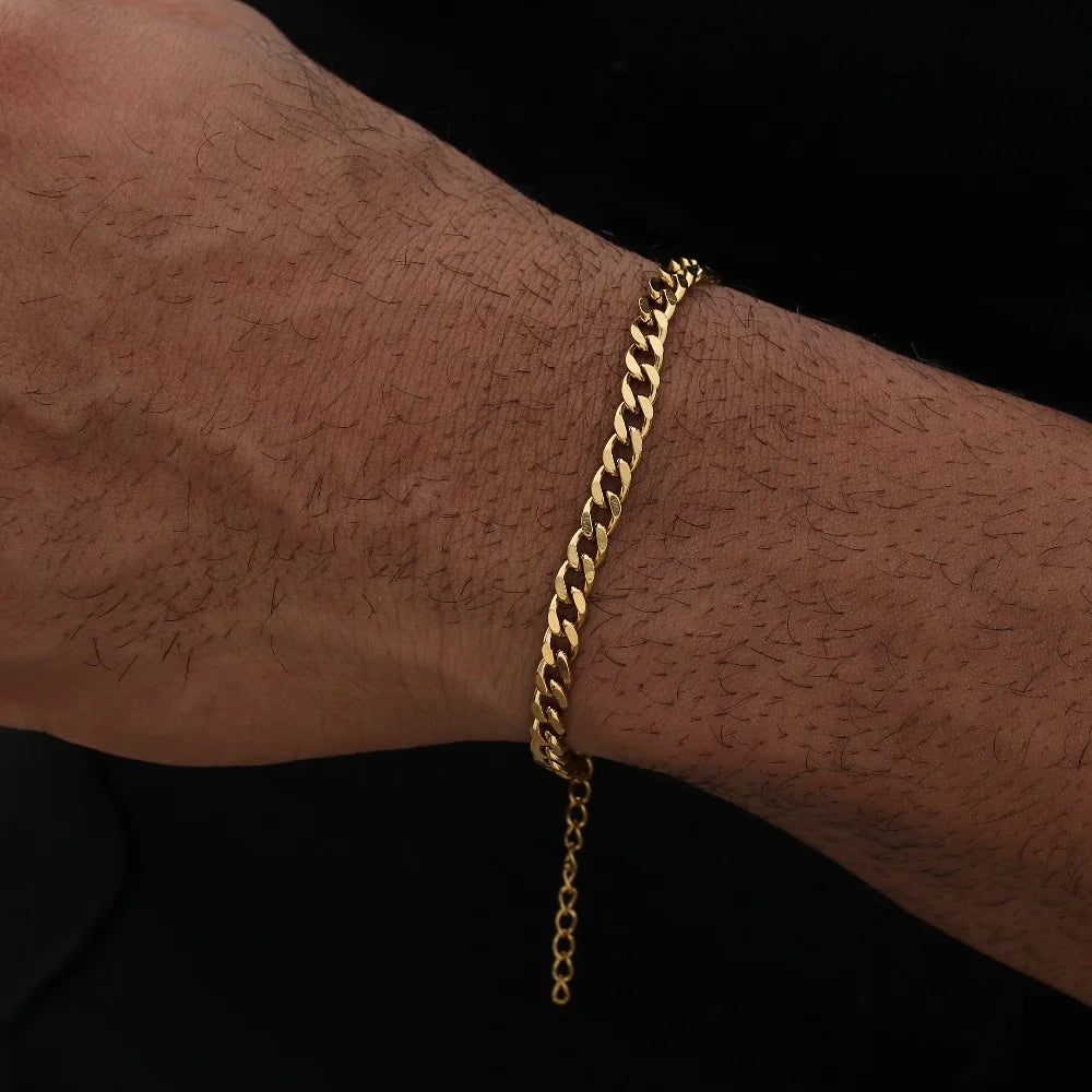 A close-up of a man's wrist wearing a gold stainless steel Cuban link bracelet.