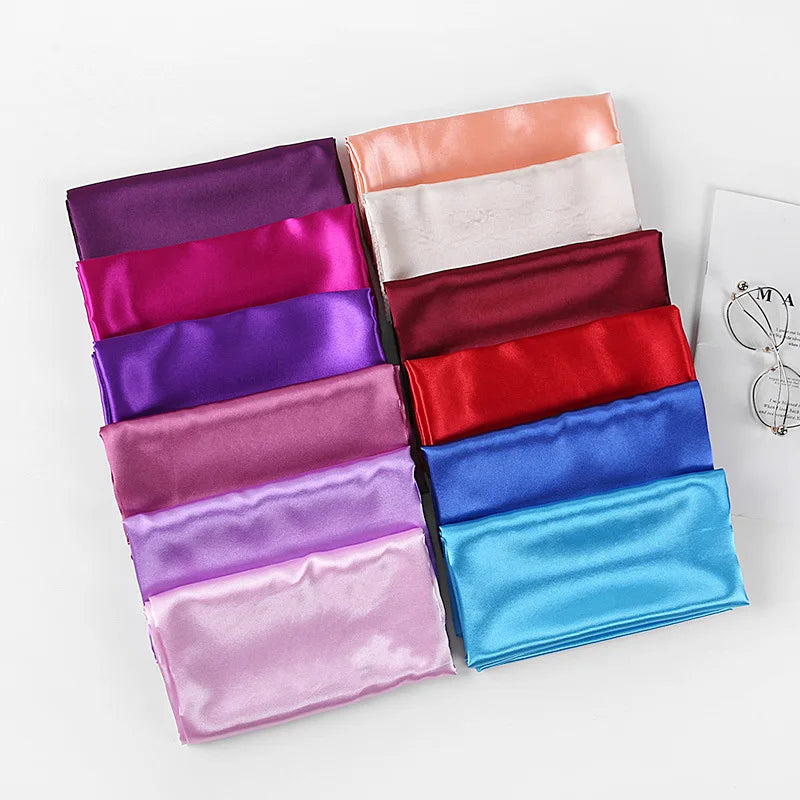 Una pila de pañuelos de seda satinada de varios colores, incluyendo tonos morados, magenta, rosa y azul.