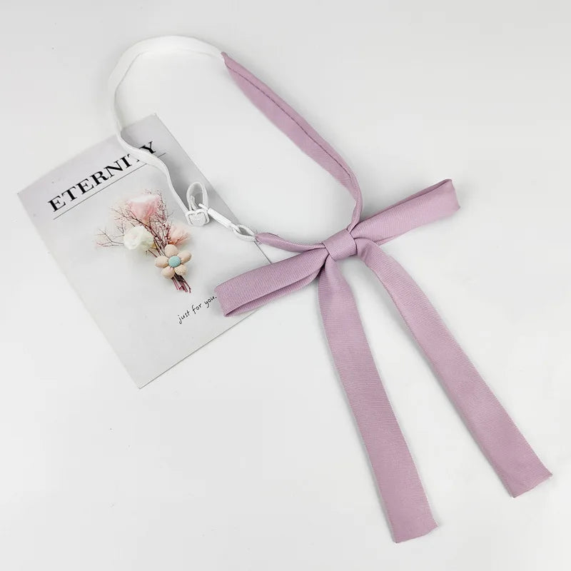 A lavender ribbon tie set with a delicate floral accent and a small charm, presented on a white card.