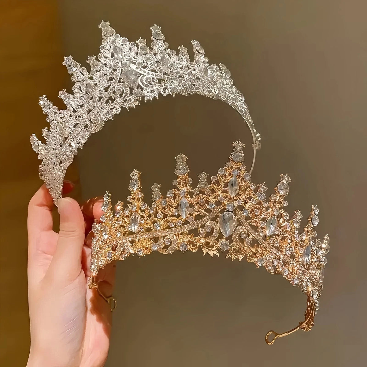 Primer plano de una elegante diadema de tiara de pedrería barroca para novia, sostenida por una mano.
