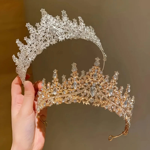 A close-up of an elegant Baroque rhinestone bridal tiara headband being held by a hand.