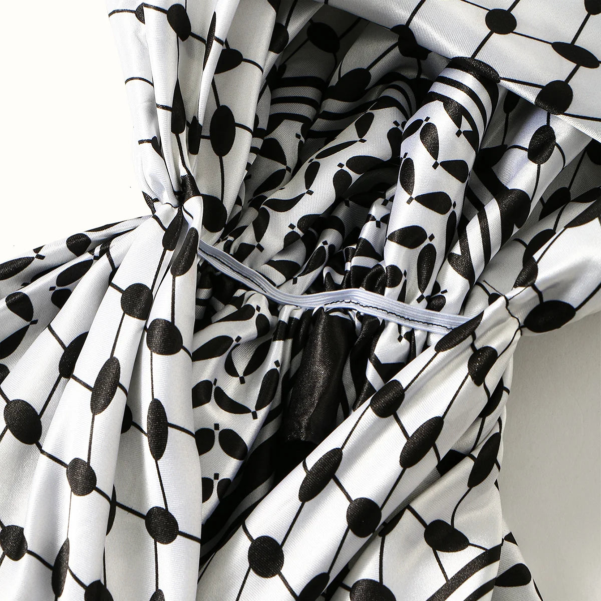 A close-up of a white and black patterned satin silk hijab fabric draped around a person's head.