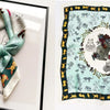 A silk scarf featuring a floral print with gold accents and various animal motifs on a light mint green background.