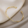 A minimalist gold-tone twisted cuff bangle resting on a neutral beige fabric.