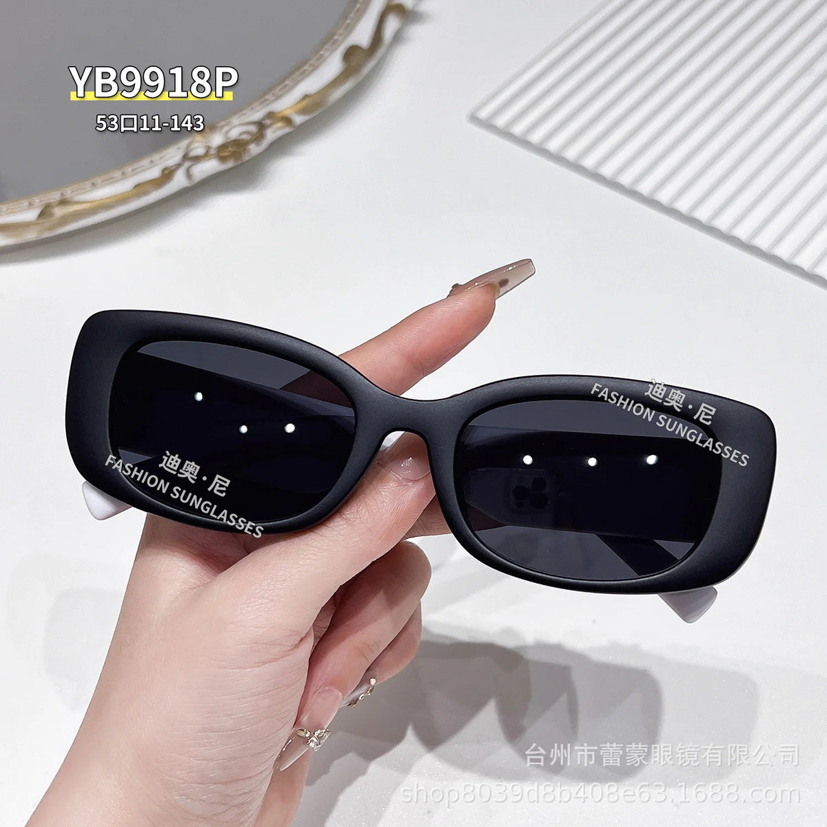 A hand holds a pair of black fashion sunglasses with dark lenses and black frames against a white background.