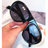 A hand holds a pair of black vintage gradient leopard print sunglasses against a white background.