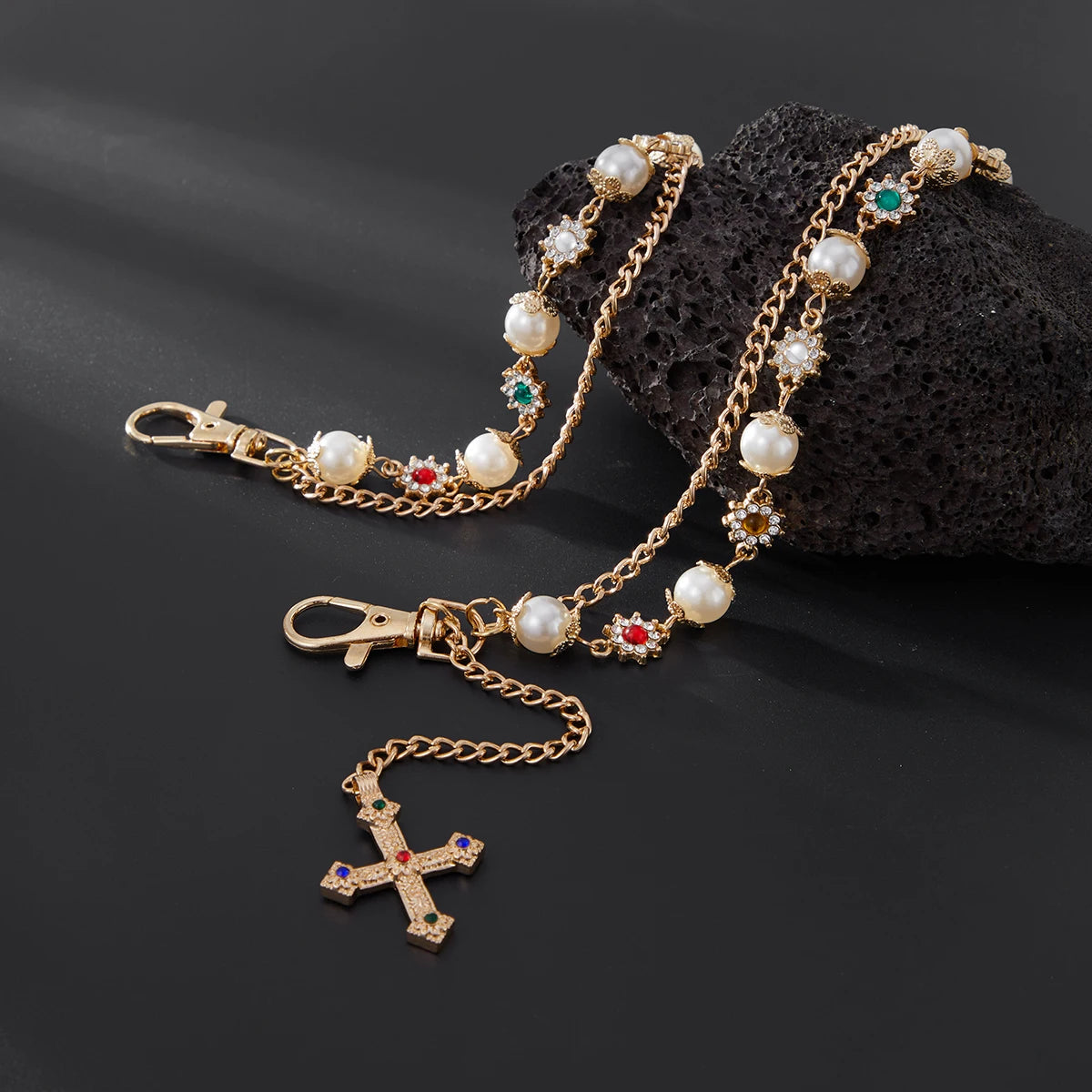 Gold chain necklace with pearl and ruby accents, featuring a cross pendant on a black stone.