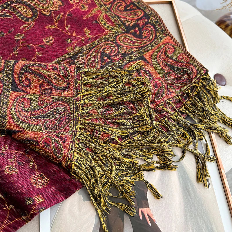 A close-up of a deep red and gold bohemian paisley tassel shawl draped on a light surface.