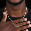 Gros plan d'une main portant un collier de chaînes cubaines en acier inoxydable sur fond sombre.