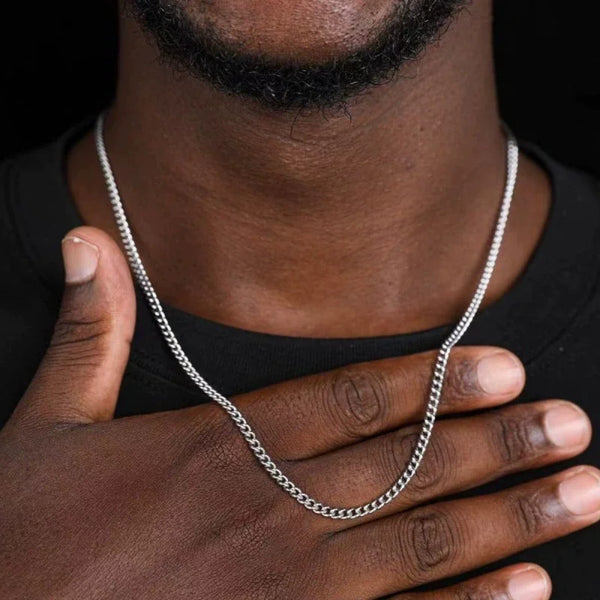 A close-up of a man's hand wearing a stainless steel Cuban link chain necklace against a dark background.