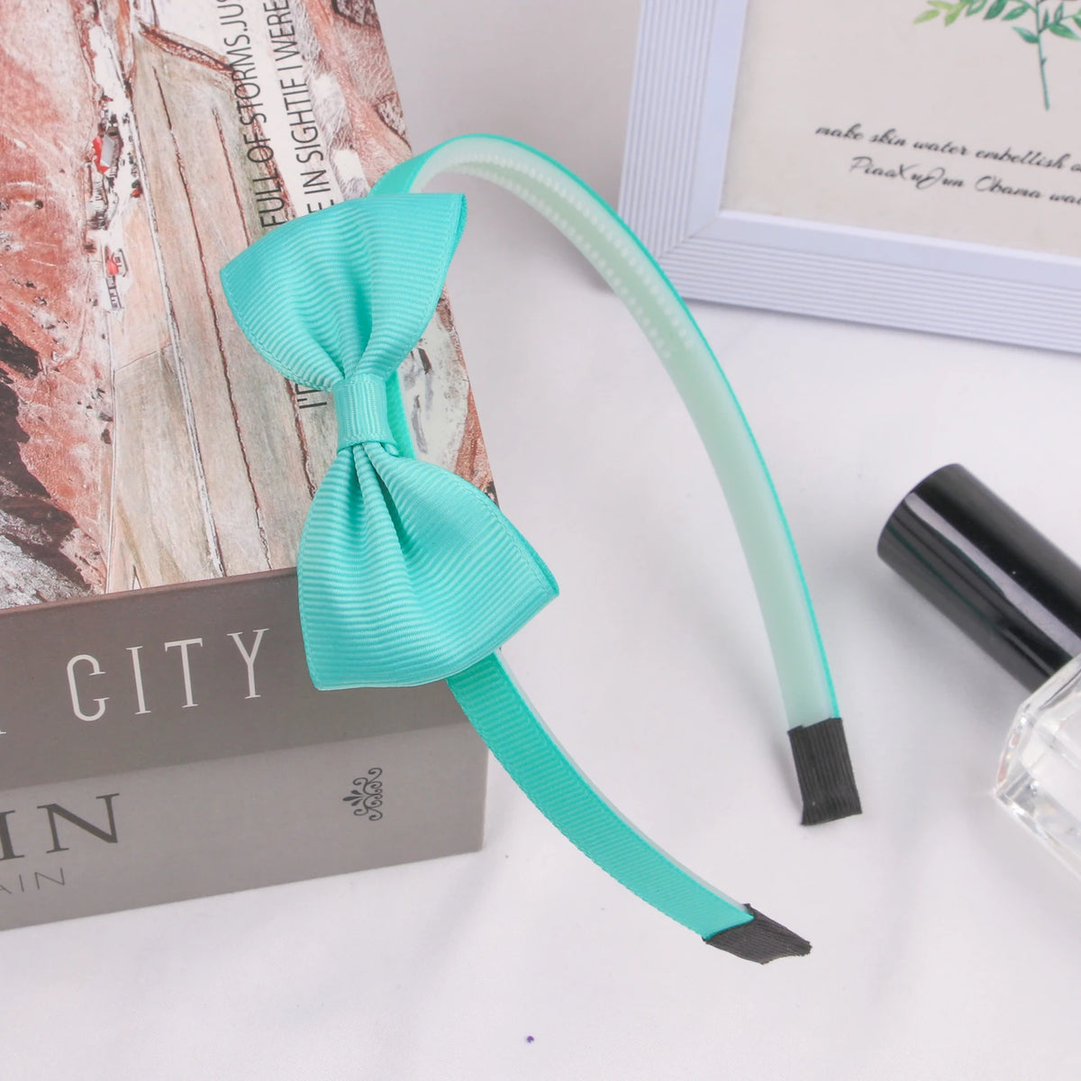 A teal grosgrain ribbon hair bow is displayed next to a box and a white frame.