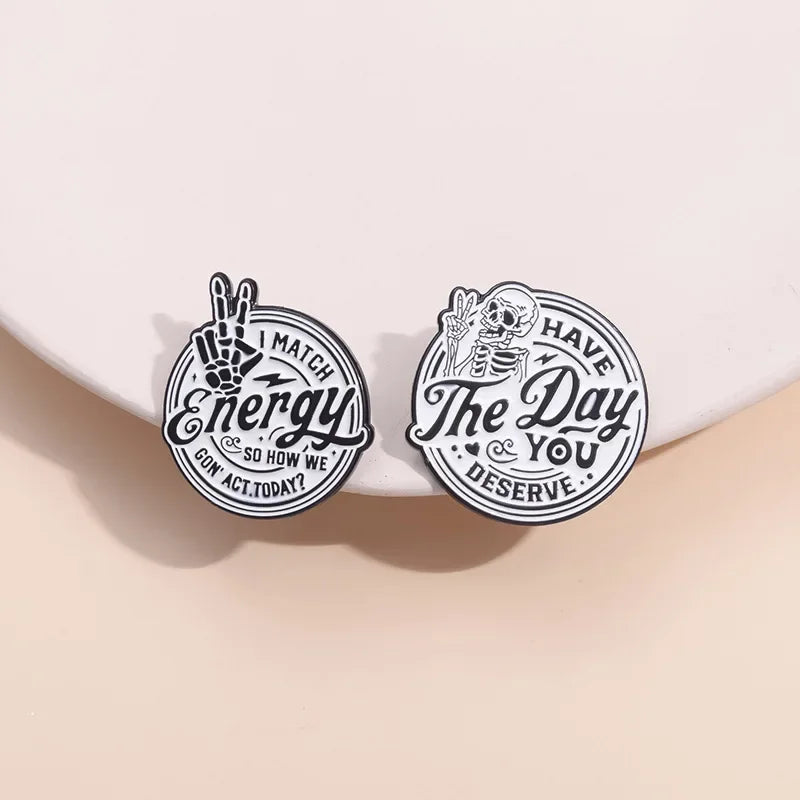 Two circular enamel lapel brooches featuring text and hand imagery on a light background.