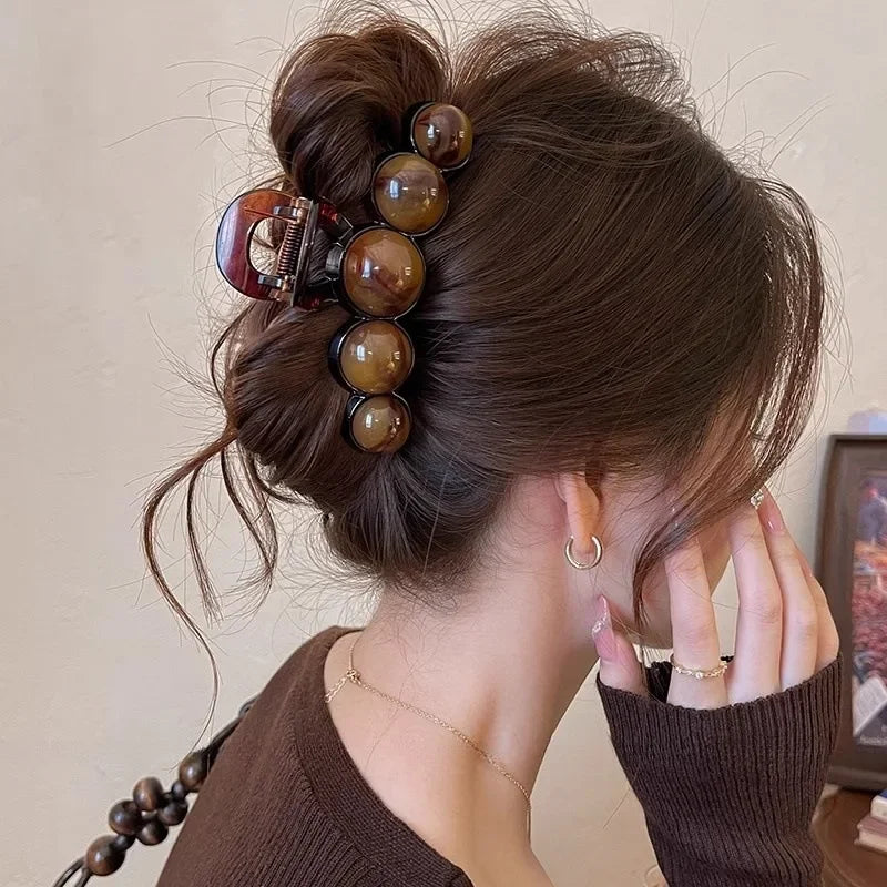 Dunkelbraunes Haar einer Frau in eleganter Hochsteckfrisur mit Retro-Gradienten-Perlen-Haarklemme aus Bernstein und Tortois.
