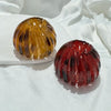 A pair of elegant, faceted horsetail hair clips in amber and deep red glass resting on a white surface.