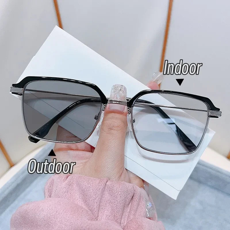 Une main tient une paire de lunettes à verres photochromiques, montrant les conditions de lumière intérieure et extérieure.