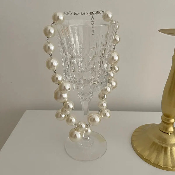 A clear glass decanter or vase decorated with a pattern of leaves and adorned with strands of white faux pearls.