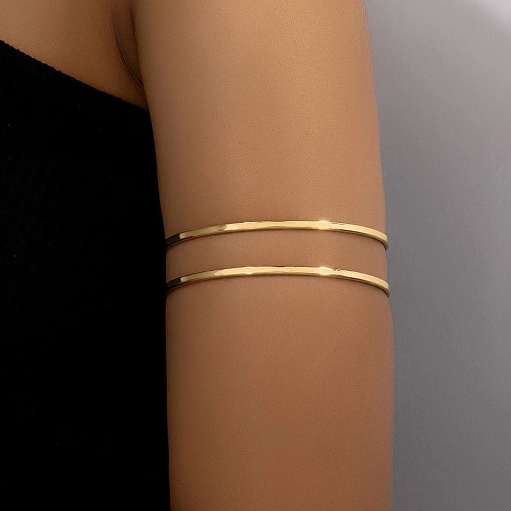 A close-up of a person's arm showing two stacked gold-plated swirl cuff bracelets on the wrist.